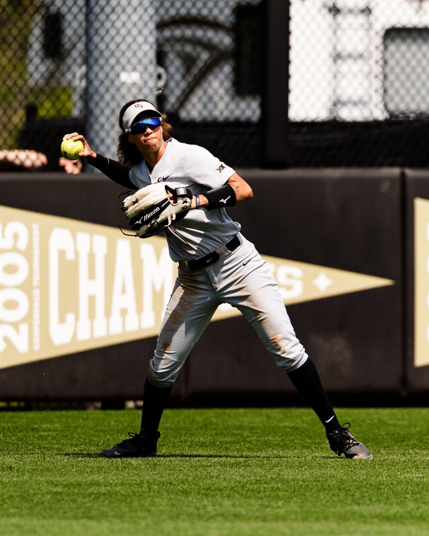 Zoe Calvez in a UCF road uniform, throwing to first from the outfield grass
